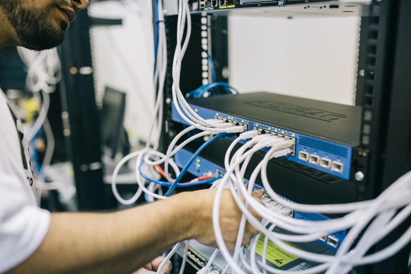 Técnico trabajando físicamente sobre las conexiones de red de un rack de infraestructura empresarial. Fotografía de referencia.